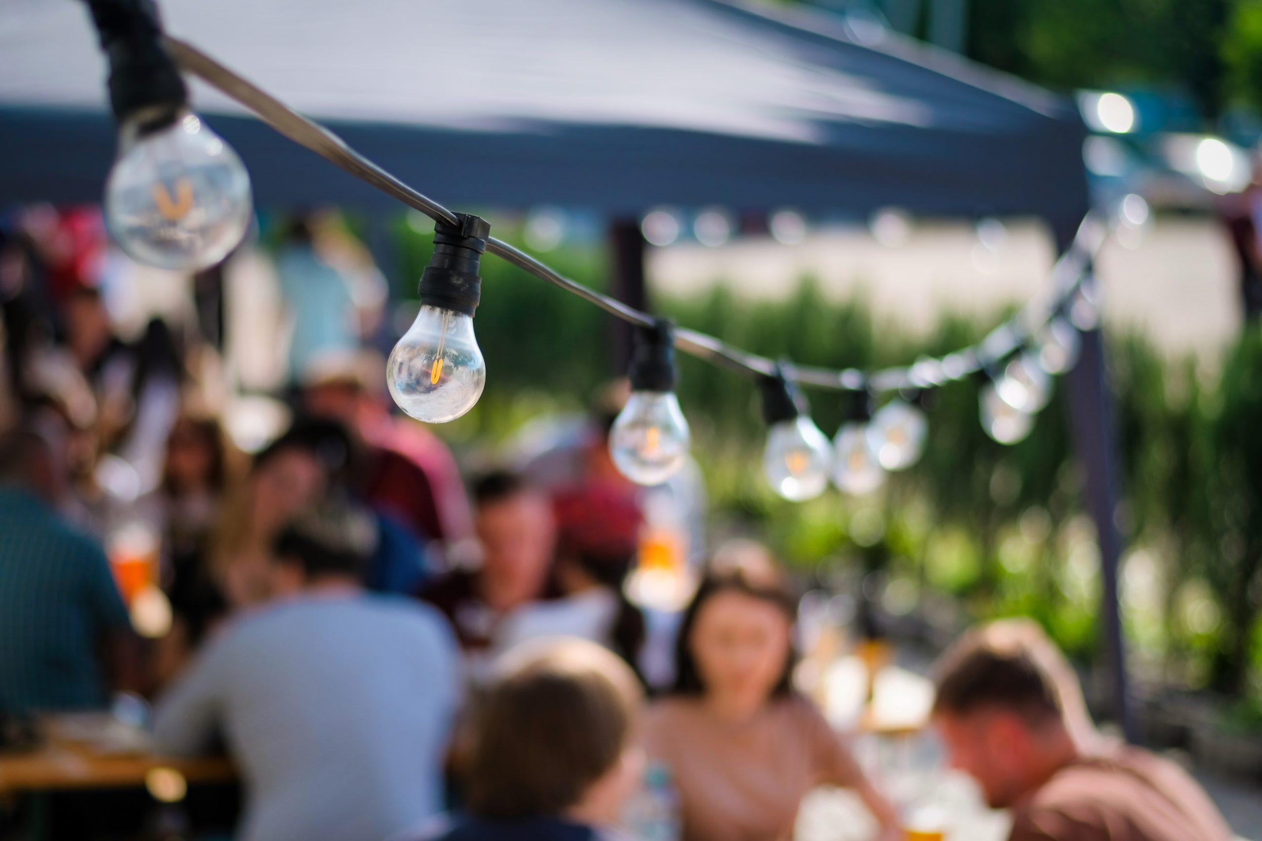 Outdoor gathering with people seated at tables under string lights
